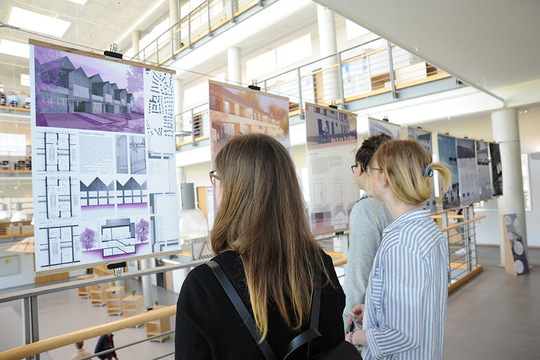 Besucher*innen des Tags der offenen Tür am Fachbereich Architektur blicken auf Plakate mit Entwürfen von Gebäuden