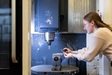 Ein Bild, das eine Studentin zeigt, die an einer Maschine mit Bohrvorrichtung arbeitet.