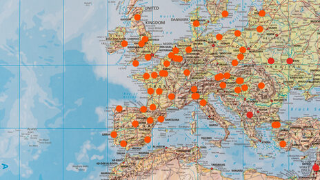 Close-up of a large world map on which places are marked with orange dots.