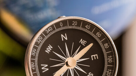 Foto eines Kompass, im Hintergrund sehr verschwommen ein Globus.