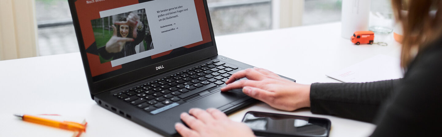 Foto über die Schulter einer Frau, die am Laptop arbeitet. Auf dem Laptop ist die Folie einer Präsentation mit der Überschrift „Noch offene Fragen?“ aufgerufen.