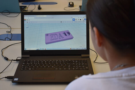Ein Mädchen schaut auf einen Laptop, den den Entwurf für einen Schlüsselanhänger zeigt mit dem Namen Eda.