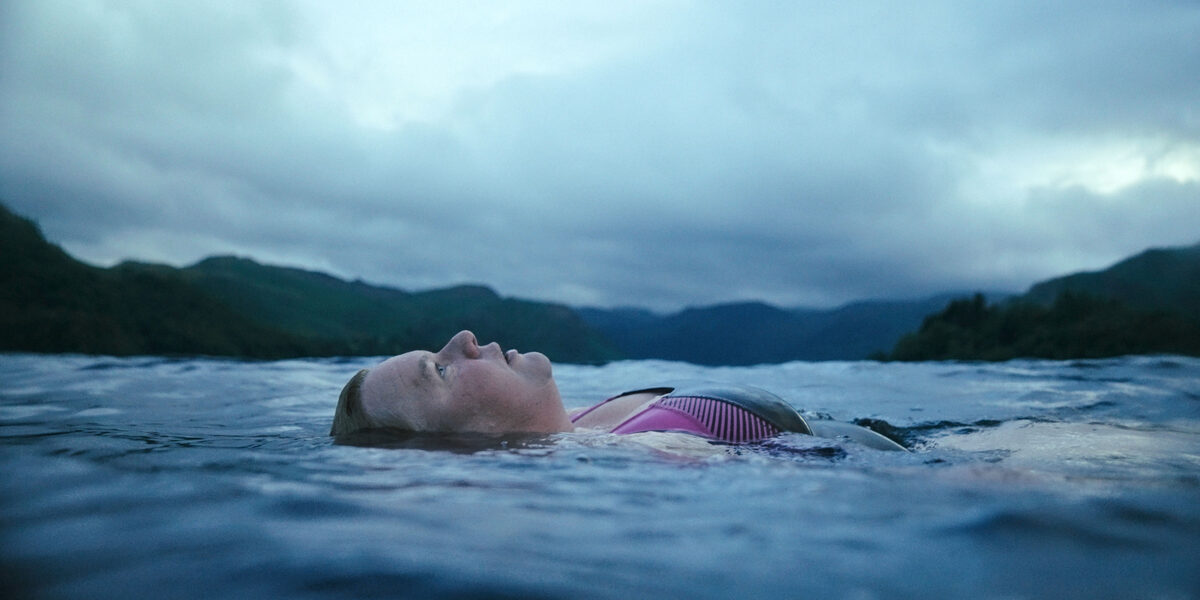 A woman swims with her back in a large body of water.