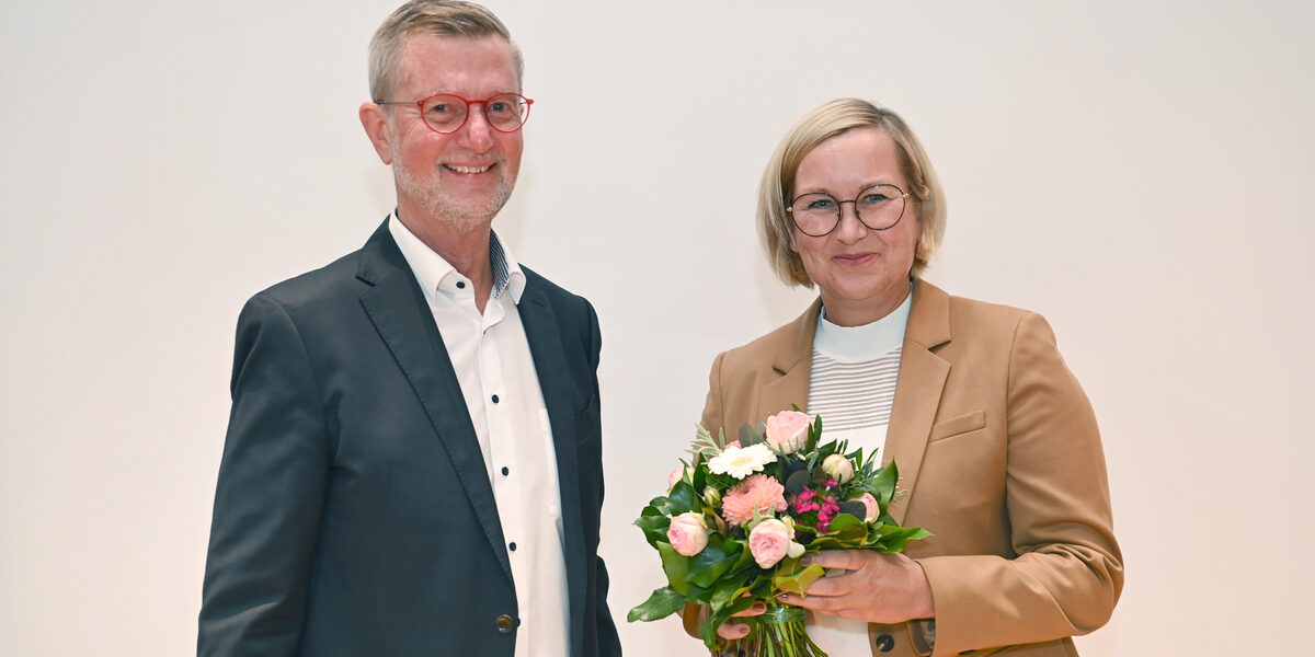 A male read person stands next to a female read person holding a bouquet of flowers.
