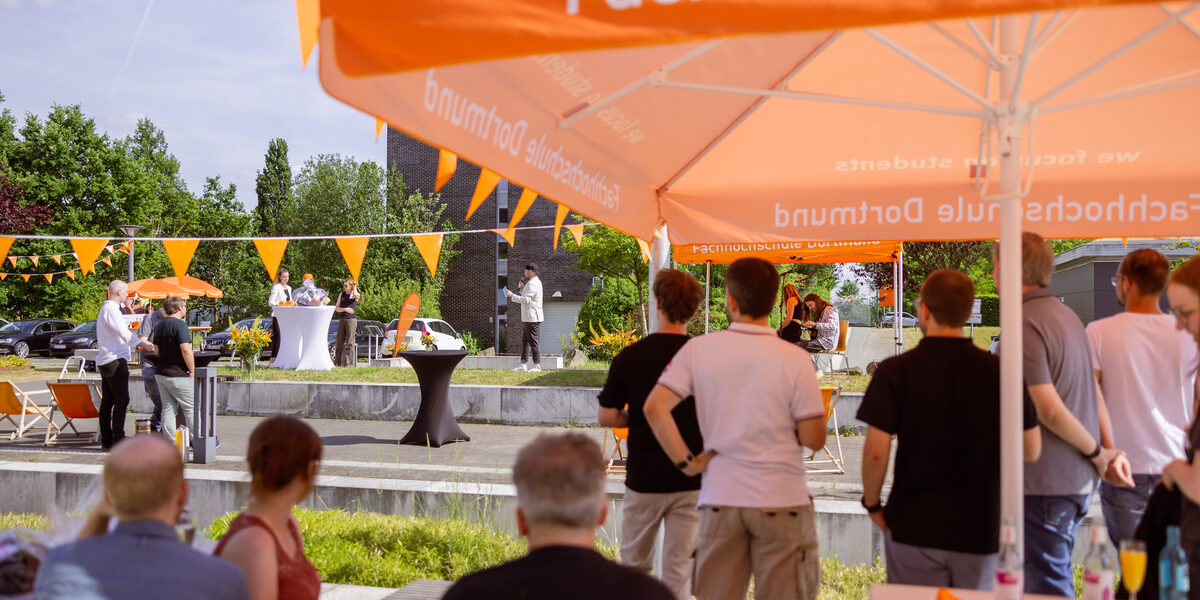 Impression des Sommerfests 2023. Menschen stehen auf dem Campus Emil-Figge-Straße und schauen das Bühnenprogramm an.