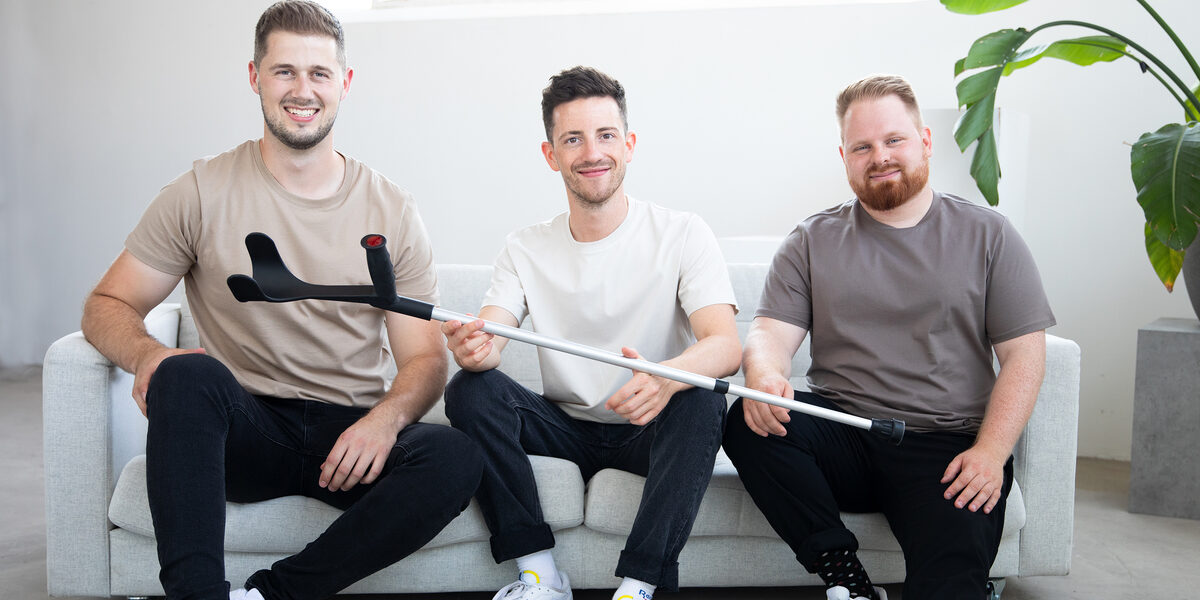 Three people are sitting on a sofa and holding a crutch.