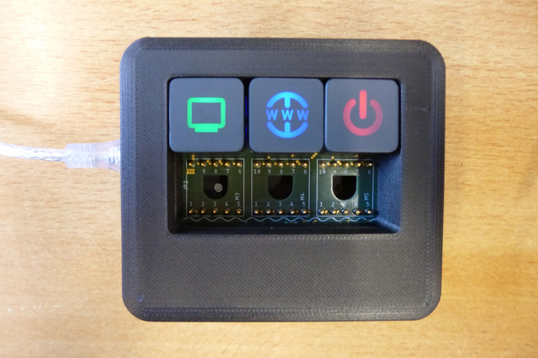 Foto eines frei konfigurierbaren Bedienelements mit drei Knöpfen und verschiedenfarbig leuchtenden Symbolen darauf.