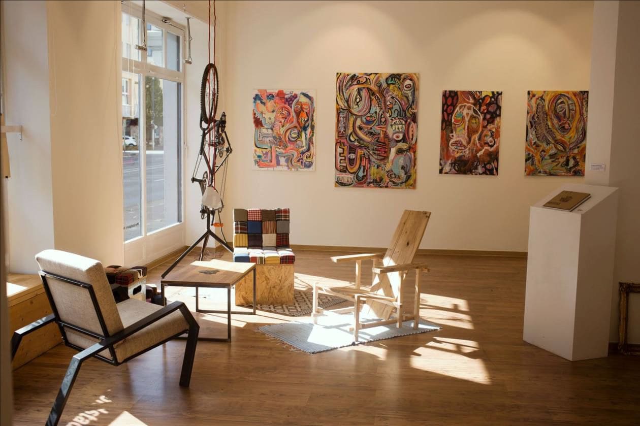 Innenaufnahme der Nordstadtgalerie: Ein Raum mit großen Fenstern, in dem künstlerische Möbel und Skulpturen stehen und gemalte Bilder hängen