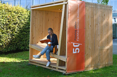 A wooden slatted construction in the shape of a cube, with a seat and backrest.