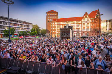 On a square in front of the old town hall, countless people stand in front of a barrier.