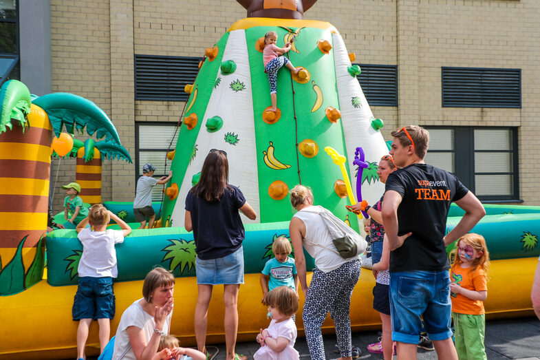 Adults and children stand in front of a bouncy castle. There are several children on this bouncy castle.