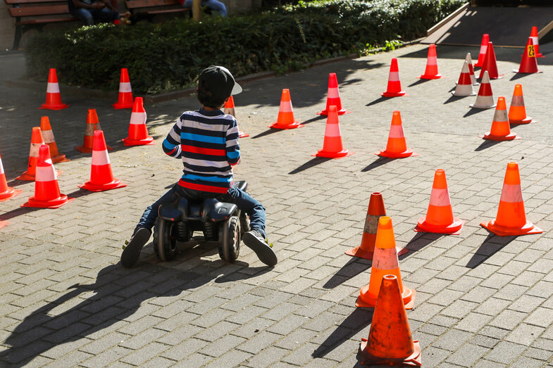 A child sits on a bobby car and drives through a course with cones.