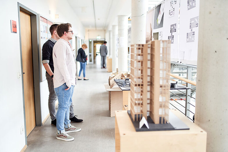 Zwei Personen blicken auf Ausstellungsstücke auf der Werkschau/der Abschlussfeier am Fachbereich Architektur
