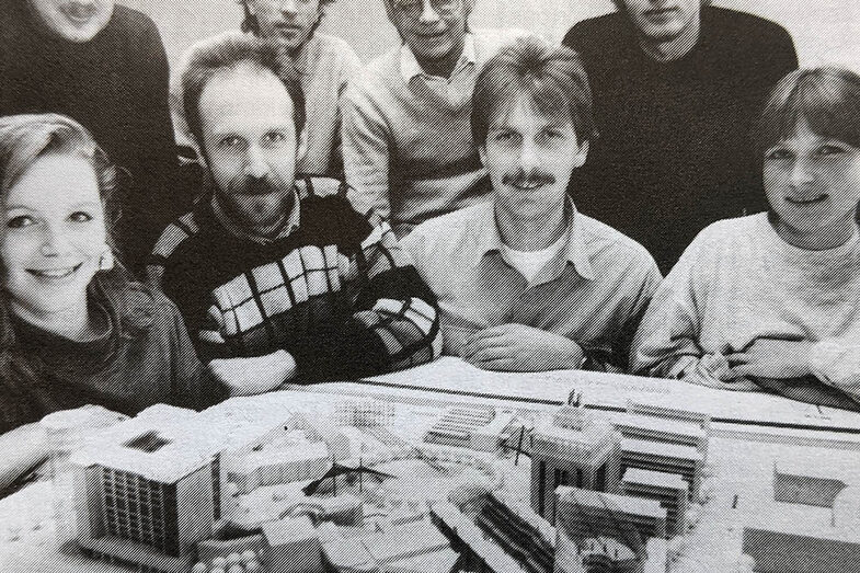 A group of people squat around an architectural model and look into the camera. The Dortmunder U is clearly visible on the model.