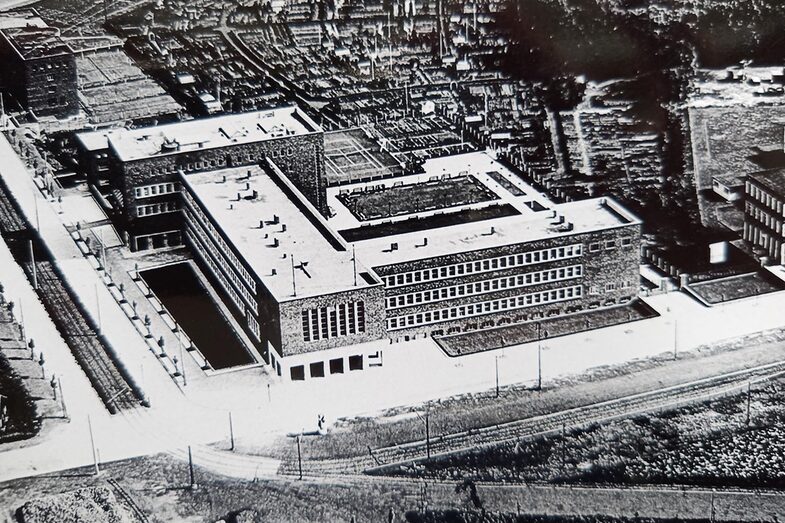 The black and white photo shows a large complex of buildings. Industry can be seen to the right of it, the Bundesstraße 1 in the foreground is only a narrow road.