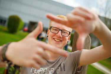 Foto eines Studenten, der mit Zeigefingern und Daumen vor sich ein Quadrat formt und dadurch guckt.