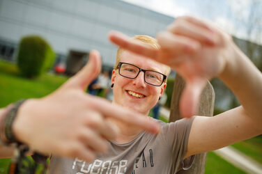 Photo of a student forming a square with his index fingers and thumb in front of him and looking through it.