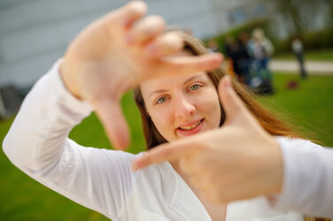 Foto einer Studentin, die mit Zeigefingern und Daumen vor sich ein Quadrat formt und dadurch guckt.