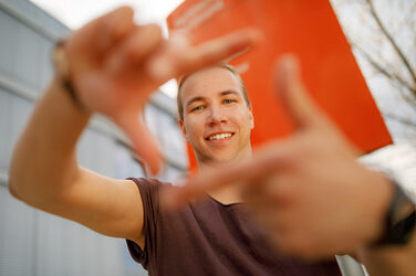 Photo of a student forming a square with his index fingers and thumb in front of him and looking through it.