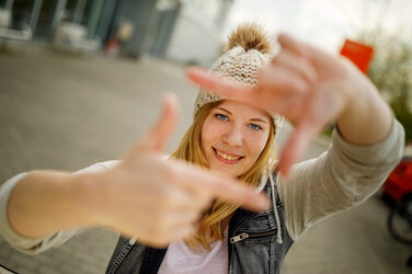 Foto einer Studentin, die mit Zeigefingern und Daumen vor sich ein Quadrat formt und dadurch guckt.