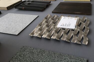 Seitlicher Blick von oben auf einen Tisch mit ausgewählten Materialmustern im Rahmen der Ausstellung „Material World“. Die Muster aus Metall, Stoffen und Holz sind groß und quadratisch.