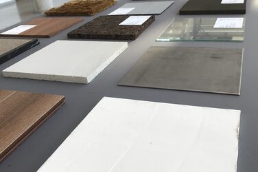 Auf einem Tisch im Foyer des Fachbereichs Architektur werden verschiedene Materialmuster präsentiert. Im Vordergrund liegen Muster aus Grantit, Stein, Glas und Holz.