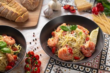 Spaghetti on a dark plate on a table, surrounded by other ingredients.