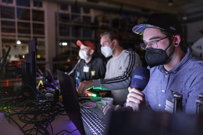 Three technicians sit in front of several laptops and monitors.