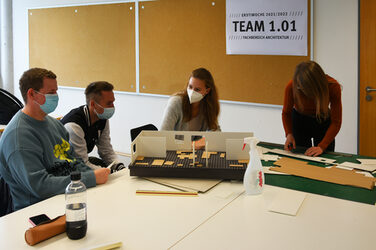 Vier Personen sitzen um einen Tisch und planen den Grundriss für die WG mit einem Pappmodell.