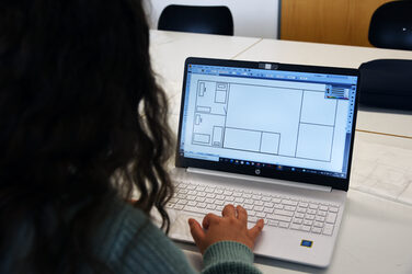 Eine Person sitzt an einem Laptop. Auf dem Bildschirm ist die Zeichnung des Grundrisses der zu planenden WG zu sehen.