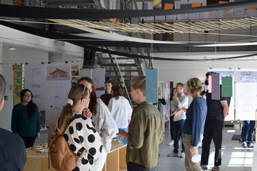 Studierende bei der Ausstellungeröffnungs im Foyer zwischen Modellen und aufgehängten Plänen.