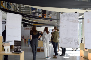 Studierende bei der Ausstellungeröffnungs im Foyer zwischen Modellen und aufgehängten Plänen.