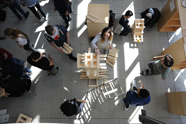 Besucher*innen des Tags der offenen Tür am Fachbereich Architektur bauen einen Turm aus Holzblöcken