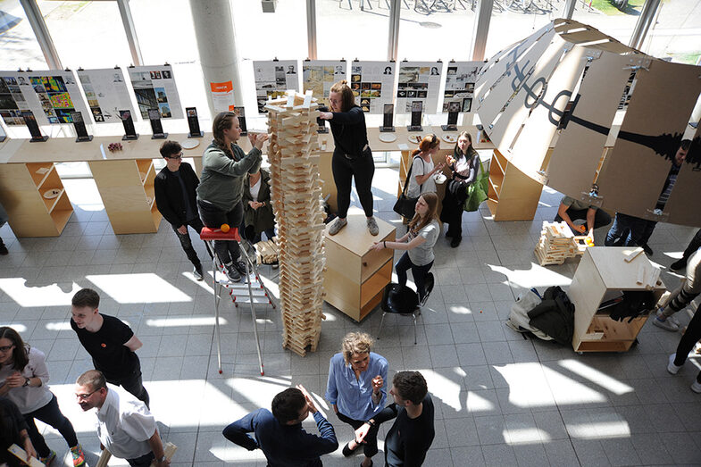 Besucher*innen des Tags der offenen Tür am Fachbereich Architektur bauen einen Turm aus Holzblöcken