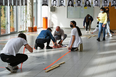 In einem Foyer knien mehrere Erstsemester-Studierende auf dem Boden und kleiben Erstsemester kleben den Grundriss ihrer WG mit neon-orangenem Klebeband.