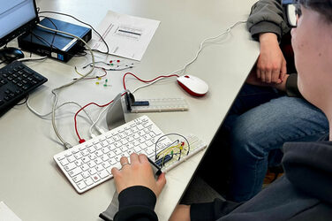 A computer keyboard and cables with technical kits lie on a table. Two people are sitting to the right.