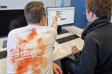 Two people are sitting at a table, one of them is showing the other something on a screen.