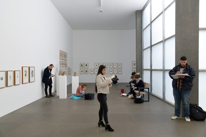 Personen sitzen und stehen in einer Galerie und halten Blöcke und Stifte in den Händen.