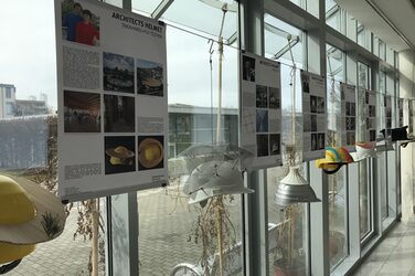 The picture shows four explanatory posters with the corresponding architects' helmets, as they hang in the foyer of the Faculty of Architecture. For example, they are decorated with a bamboo platform running all the way around in the style of Takaharu and Yui Tezuka.