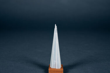 In this picture, a 3D-printed model made of translucent plastic, about three centimetres high, is presented on a thin wooden base. It shows The Shard building in London, Great Britain. As the name suggests, the skyscraper has a shard shape that tapers sharply towards the top.
