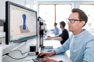 Photo of a man at the computer creating a model for the 3D printer.