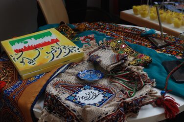 Kulturstand Iran: Bunte Tücher auf einem Tisch, daneben bemalte Leinwände mit Schriftzeichen.