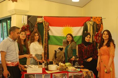 Sechs Personen stehen um den dekorierten Tisch am kurdischen Kulturstand und blicken in die Kamera.