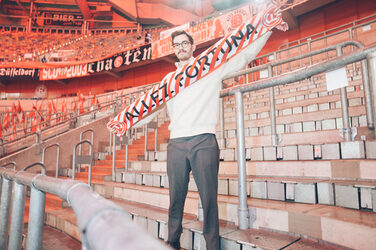 Eine Person steht am Spielfeldrand in einem Stadion und präsentiert einen Fanschal.