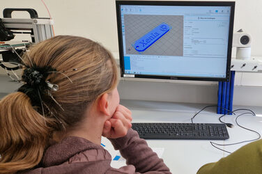 A person is looking at a screen. It shows a model of a name badge with the inscription Xenia.