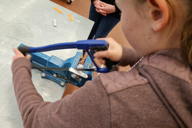 A person is sawing with both hands on a nameplate attached to a workbench.