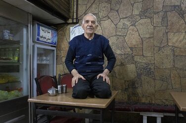 A person with short gray hair kneels on the tabletop in a snack bar.