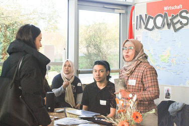 Vier junge  Menschen in einem Gespräch an einem internationalen Messestand aus Indonesien beim "Marktplatz der Möglichkeiten"__Four young people in conversation at an international trade fair stand from Indonesia at the "Marketplace of Opportunities"