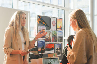 Zwei junge Frauen unterhalten sich im Sonnenschein an einem internationalen Messestand beim "Marktplatz der Möglichkeiten"__Two young women chat in the sunshine at an international trade fair stand at the "Marketplace of Opportunities"