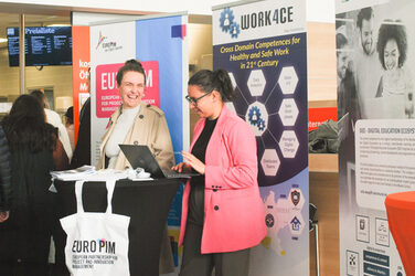 Two young women are laughing and talking at a laptop at a booth, at the "Marketplace of Opportunities"__Two young women are laughing and talking at a laptop at a booth, at the "Marketplace of Opportunities"